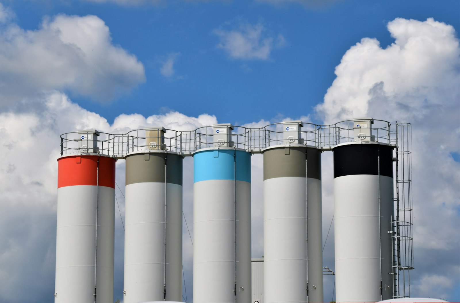 Tall industrial silos with colored bands under a cloudy blue sky