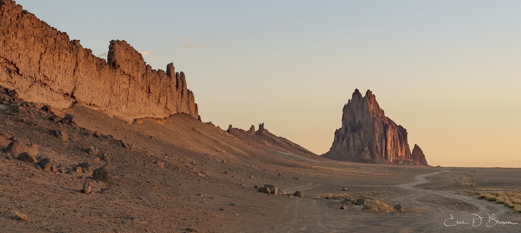 Shiprock (Tsé Bitʼaʼí) rising from the flat New Mexico desert, lit warm on its east face at dawn.